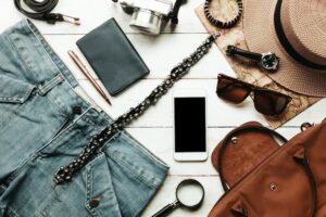 acessorios-de-vista-superior-para-viajar-com-conceito-de-vestuario-feminino-telemovel-relogio-saco-chapeu-mapa-camera-colar-calcas-e-oculos-escuros-na-mesa-de-madeira-branca_1921-106 (1)