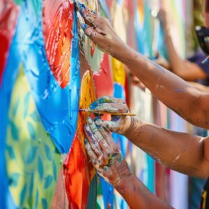 maos-de-artistas-pintando-um-mural-vibrante-juntos-colaboracao-criativa-com-pinceis-e-pinturas-coloridas-em-um-cenario-ao-ar-livre_1099133-17690